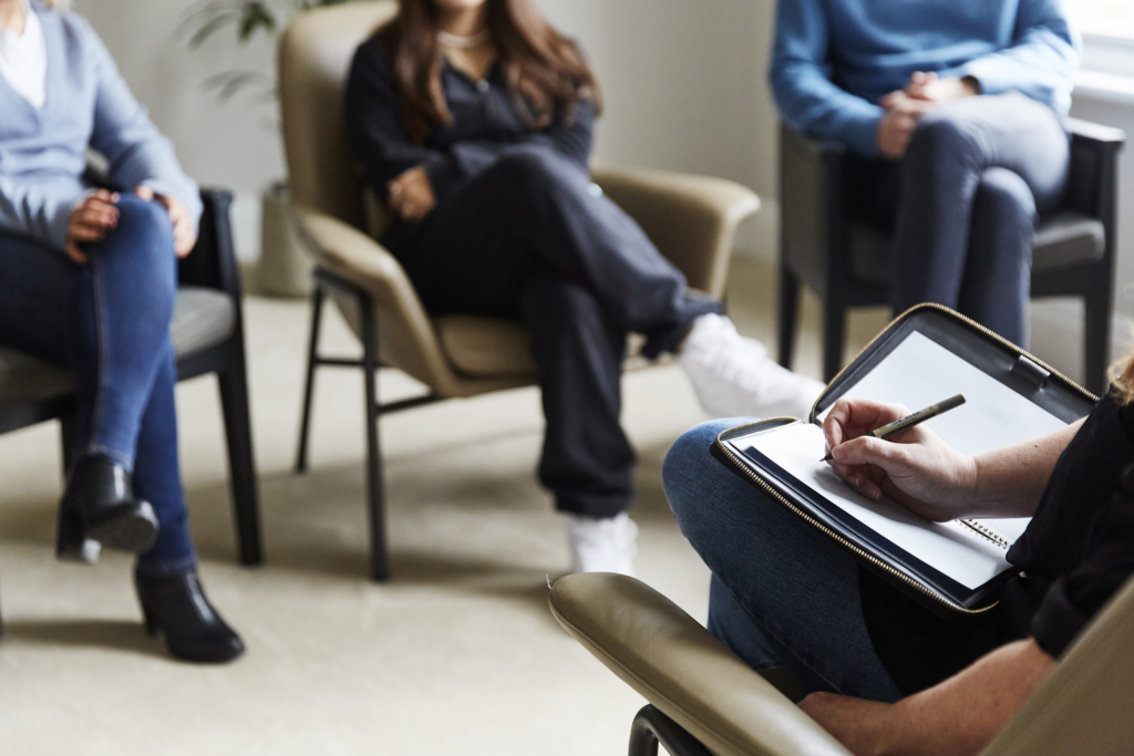 Group therapy session at The Chelsea Psychology Clinic in London, with participants seated in comfortable chairs and openly discussing mental health support in a relaxed environment.