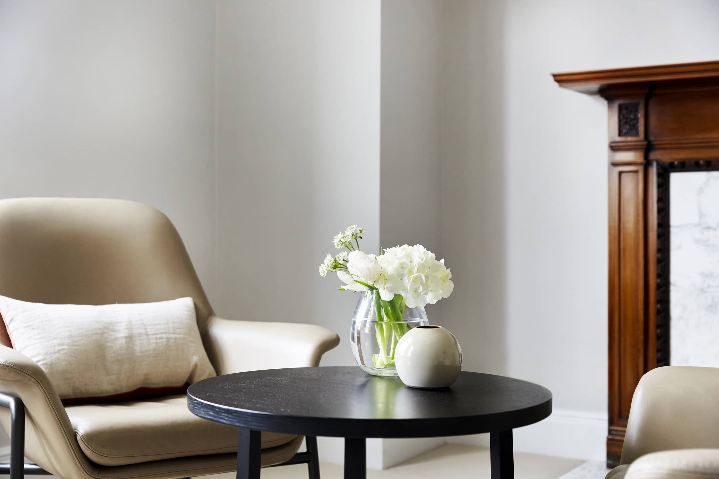 Serene therapy room at The Chelsea Psychology Clinic, featuring a comfortable beige armchair, sleek black table with fresh flowers and a fireplace, creating a welcoming environment for mental health support.