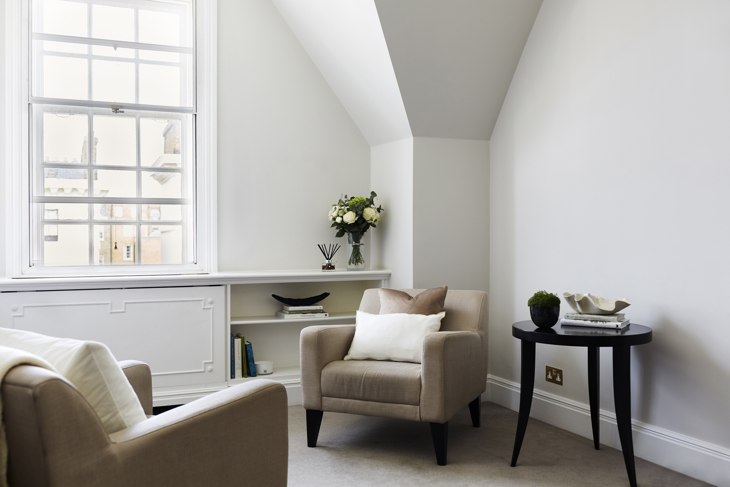 Bright, airy therapy room at The Chelsea Psychology Clinic in London, featuring a neutral-toned armchair, built-in shelves with books, and a large window letting in natural light for a calm, welcoming environment.
