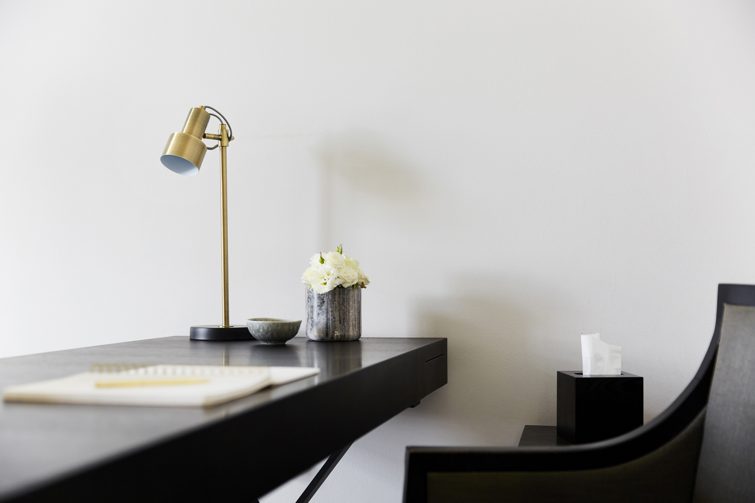 Sleek black desk with a brass lamp, white flowers and a notepad in a calm therapy office at The Chelsea Psychology Clinic in London, providing a serene, professional setting for private psychology and psychiatry.